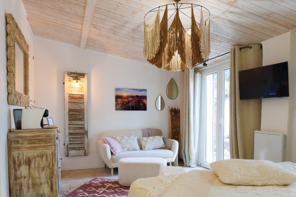 Intérieur d'un salon lumineux avec un canapé, une lampe suspendue et un téléviseur.