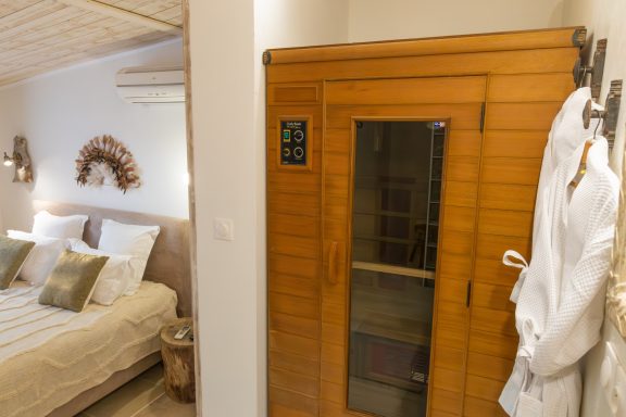 Un sauna en bois à côté d'un lit avec des draps clairs et des coussins décoratifs.