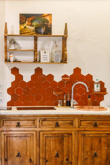 Cuisine authentique et chaleureuse – Appartement Tahaa Plan de travail en bois avec carrelage hexagonal rouge et évier moderne. Étagère en bois en haut.