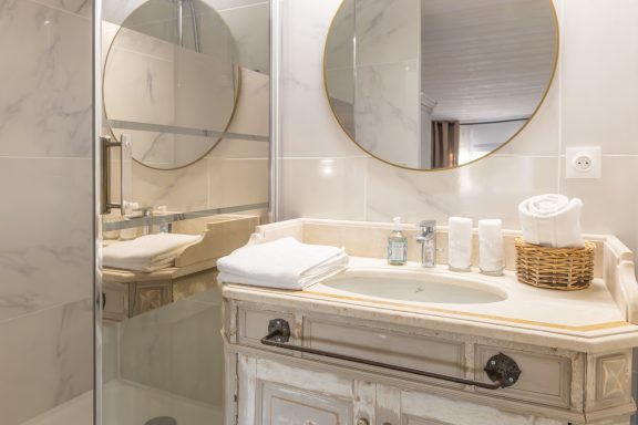 Salle de bain avec lavabo, miroir rond et serviettes blanches sur un meuble en bois.