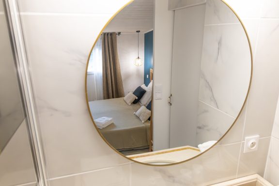 Miroir rond en or reflétant une chambre avec des coussins et des rideaux.