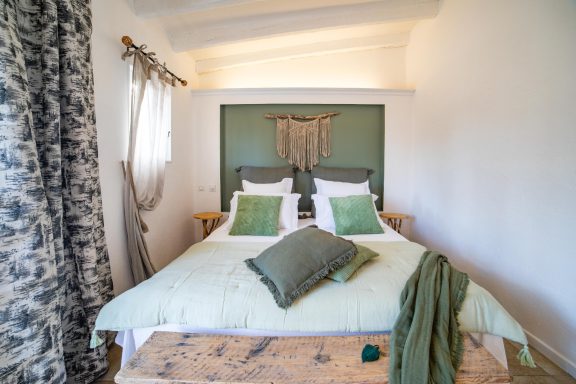 Chambre lumineuse avec un lit double, coussins verts et rideaux élégants.