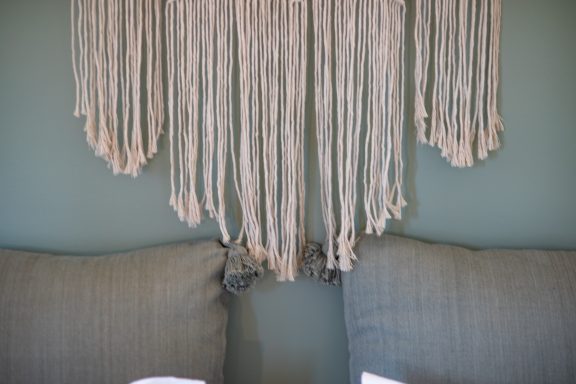 Suspension en macramé au-dessus de deux coussins sur un mur vert.