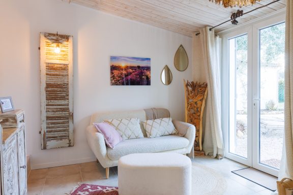 Un salon lumineux avec un canapé, un pouf et des décorations murales.