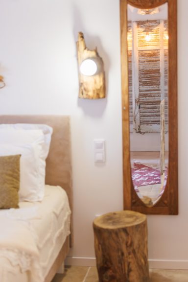 Chambre avec lit, miroir en bois et table de nuit en rondin. Éclairage chaleureux.