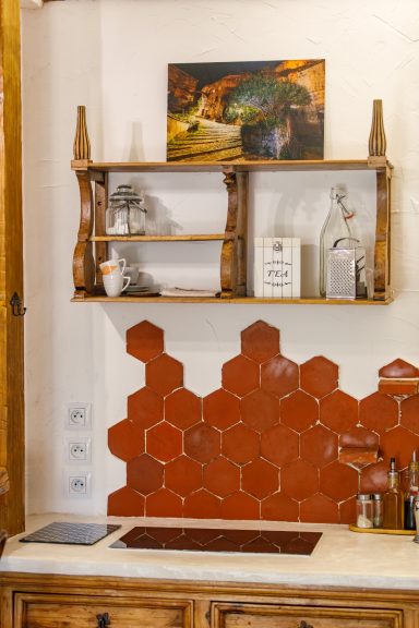 Cuisine au charme provençal de l'appartement Tahaa à La Bastide du Mûrier Mur de cuisine avec des carreaux tommette rouges et étagères en bois.