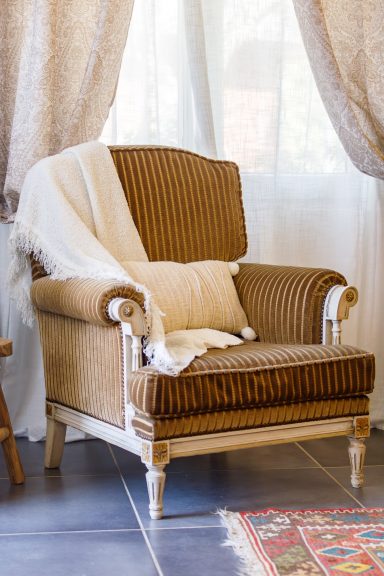 Fauteuil élégant et coin détente dans Tahaa Fauteuil en tissu rayé marron avec un plaid blanc sur le côté, près d'une fenêtre.