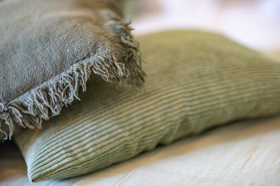 Coussins en laine avec des textures et couleurs douces, posés sur un lit.